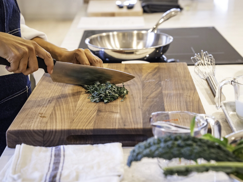 Hands are shown using a chef's knife to cut kale.